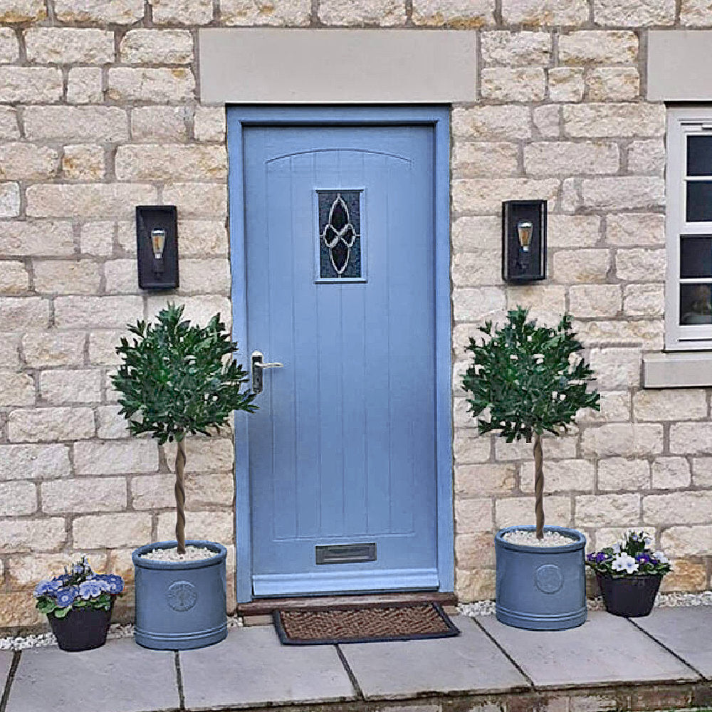 Pair of Artificial Topiary Bay Trees with Twisted Natural Trunk On Either Side of a Blue Door of  Country Home